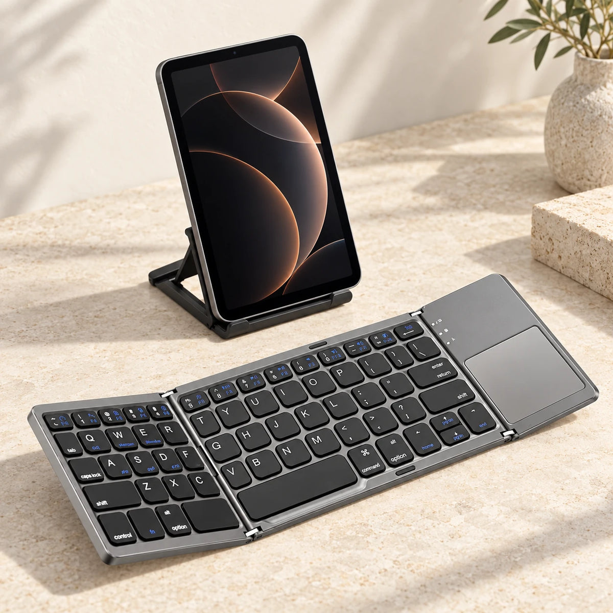 Gray wireless folding keyboard in front of a tablet on a desk.