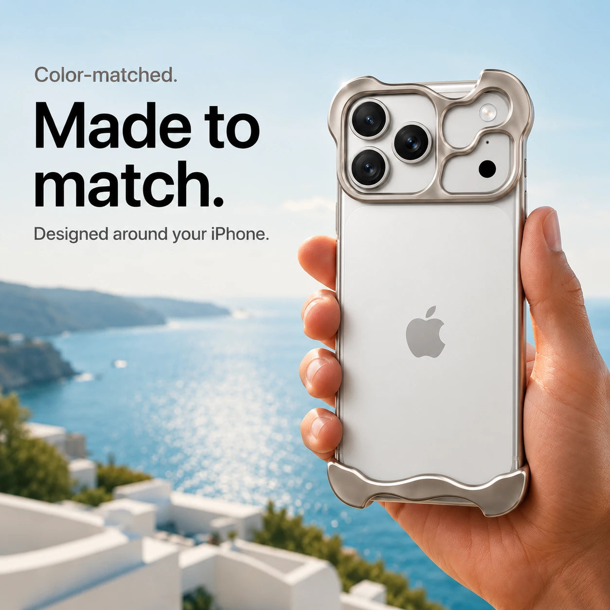 Warm gray sculpted metal phone case held in a hand above a coastal background #color_Natural Titanium