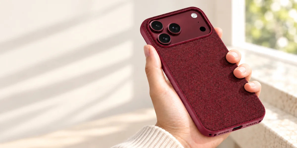 A hand holding a Burgundy woven phone case in soft window light.